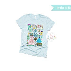 Pu&ograve; includere: Una maglietta blu chiaro con una stampa grafica colorata di vari personaggi e simboli di principesse e sirene Disney. La grafica include Ariel, Cenerentola e altri personaggi dei film Disney.