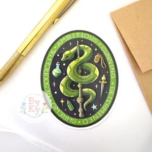 May include: A green and black sticker featuring a stylized green snake coiled around a wand. The sticker has the words "Resourceful, Ambitious, Cunning, Determined, Shrewd" around the edge. Additional elements include a potion bottle, a pendant, and a dagger.