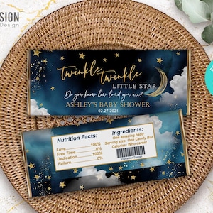 May include: Two candy bar wrappers with a celestial theme. The top wrapper reads "Twinkle Twinkle Little Star" with the text "Ashley's Baby Shower 02.27.2021". The bottom wrapper has a nutrition facts label and ingredient list.