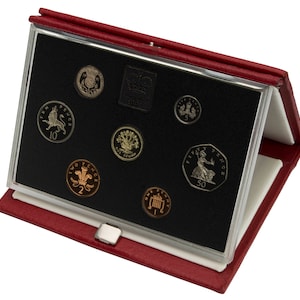 Op de afbeelding: Een rood leren muntverzamelkoffer met een zwart fluwelen interieur. De koffer bevat een set Britse munten, waaronder een munt van één pond, een munt van vijftig pence, een munt van twintig pence, een munt van tien pence, een munt van vijf pence, een munt van twee pence en een munt van één pence.