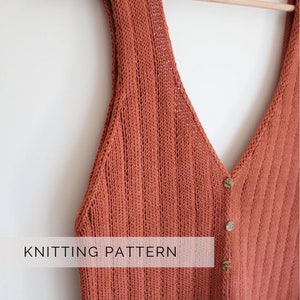Può includere: Un gilet lavorato a maglia color ruggine con scollo a V e chiusura con bottoni, appeso a una gruccia di legno. Il gilet presenta una trama a coste e le parole "KNITTING PATTERN" sono visibili. Articolo fatto a mano.