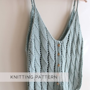 Può includere: Un top di maglia blu chiaro con chiusura a bottone e un delicato motivo traforato. Il top è appeso a un appendiabiti di legno. "Knitting Pattern" è scritto in bianco su sfondo nero.