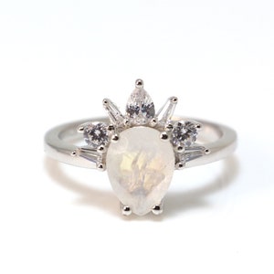 Puede incluir: Un anillo de plata con una piedra preciosa blanca en forma de pera rodeada de piedras preciosas blancas m&aacute;s peque&ntilde;as.
