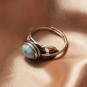 May include: A silver ring with a blue gemstone and a feather design.