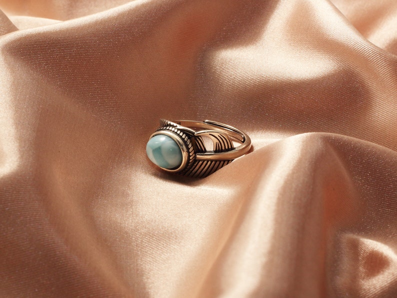May include: A gold ring with a blue oval gemstone set in a feather design.