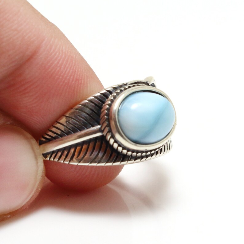 May include: A silver ring with a blue opal gemstone set in a feather design.