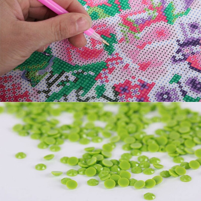 May include: Close-up of a green diamond painting kit with a pink pen and a pile of green diamond-shaped rhinestones.