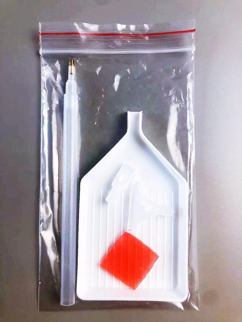 May include: A clear plastic bag containing diamond painting supplies. The supplies include a white tray with a red diamond-shaped piece, a clear plastic pen with a gold tip, and two white plastic tools.