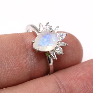 Puede incluir: Un anillo de plata con una piedra de luna en forma de pera y un halo de piedras peque&ntilde;as transparentes.