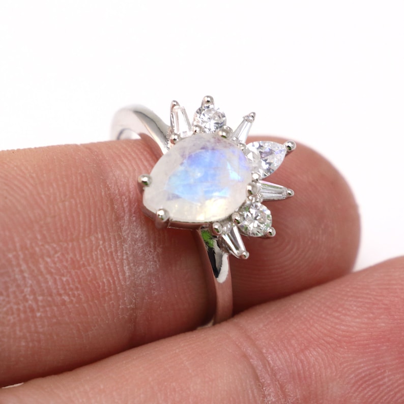 Puede incluir: Un anillo de plata con una piedra de luna en forma de pera y un halo de piedras peque&ntilde;as transparentes.