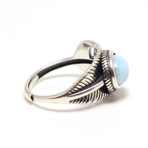 May include: A silver ring with a blue gemstone set in a detailed, ornate design. The ring features a textured band and a raised, oval-shaped stone.