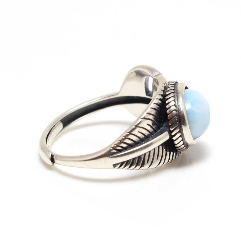 May include: A silver ring with a blue gemstone set in a detailed, ornate design. The ring features a textured band and a raised, oval-shaped stone.