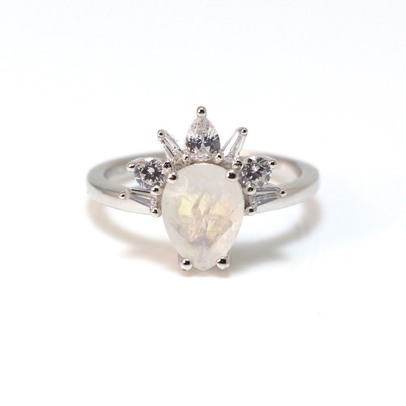 Puede incluir: Un anillo de plata con una piedra preciosa blanca en forma de pera rodeada de piedras preciosas blancas m&aacute;s peque&ntilde;as.
