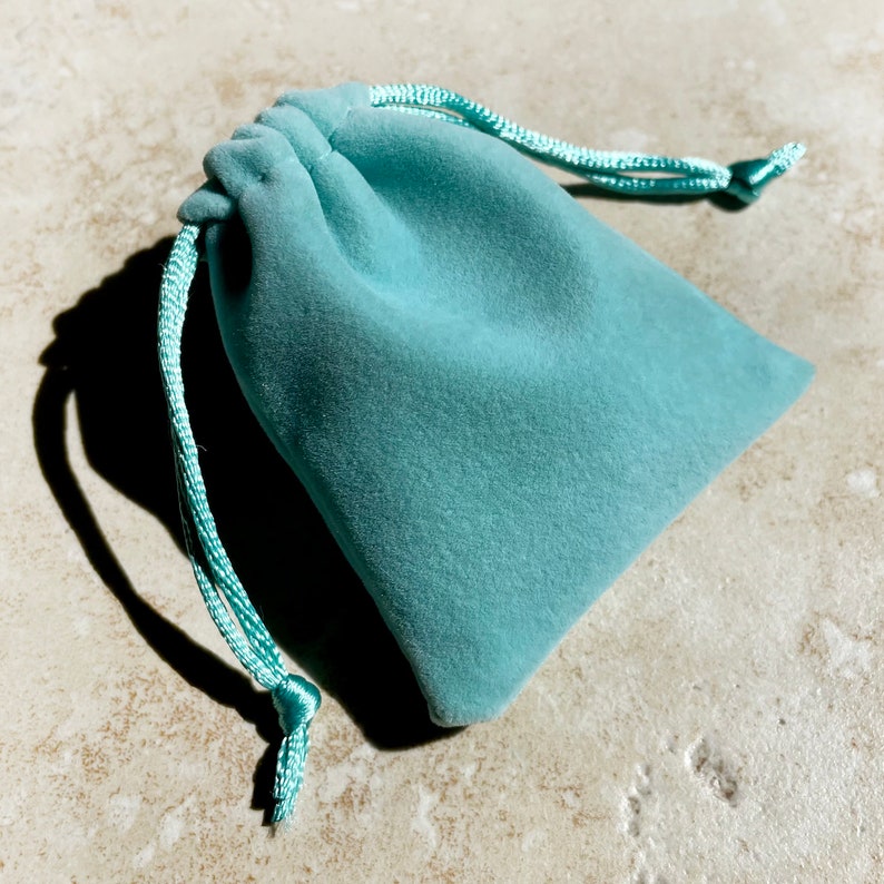 Puede incluir: Una bolsa de cord&oacute;n de terciopelo azul claro con un cord&oacute;n blanco.