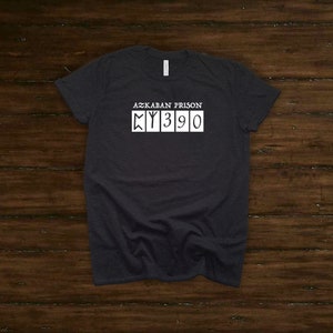 May include: A dark gray t-shirt with white text that reads "Azkaban Prison" and "MY390".