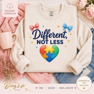 Könnte beinhalten: Cremefarbenes Sweatshirt mit dem Text "Different, NOT LESS" und einem herzförmigen Puzzledesign. Das Design umfasst eine rosa Schleife, eine blaue Schleife und Sterne. Das Sweatshirt wird mit einer rosa Tasse und einer rosa Strickdecke präsentiert.