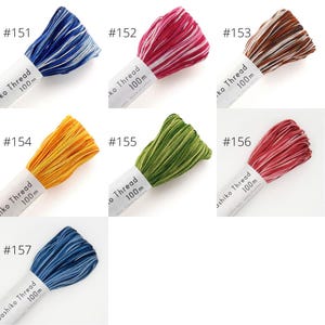 Puede incluir: Surtido de carretes de hilo para bordar de 100 m en varios colores, incluidos azul, blanco, rojo, verde, amarillo, marrón y rosa. Cada carrete está etiquetado con un número y el texto "Ko Thread" o "Ashiko Thread".