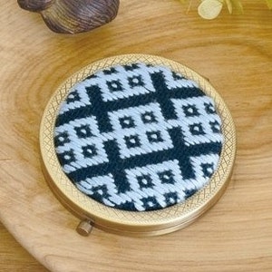 May include: A round, brass-coloured compact mirror with a black and white geometric pattern on the lid.