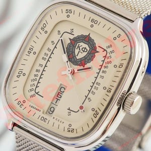 Può includere: Orologio da polso vintage con quadrante quadrato color crema e cinturino in maglia d'argento. Il quadrante presenta segni neri e rossi, un datario e un emblema dettagliato. Un orologio classico.