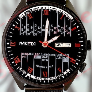 Puede incluir: Un reloj de pulsera negro con un dial de calendario y una aguja de segundos roja. La esfera del reloj presenta números romanos y un fondo negro con marcas blancas. La esfera del reloj también incluye el texto "PAKETA" y "СДЕЛАНО В СССР".