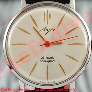 Puede incluir: Un reloj de pulsera plateado con una esfera blanca y detalles dorados. La esfera del reloj tiene una aguja de segundos roja y el texto "23 jewels Shockproof" y "MADE IN USSR".