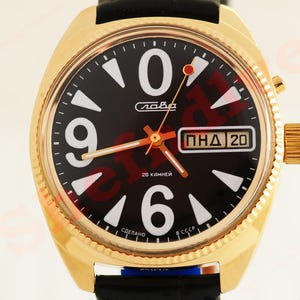 May include: A gold wristwatch with a black face, white numerals, and markers. The watch includes a date display and a black leather strap. The watch face has the text "Слава" and "26 камней".
