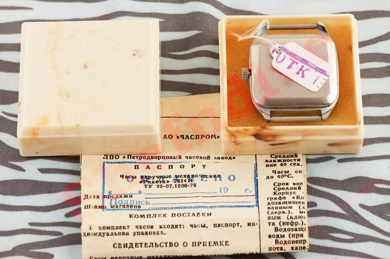 Puede incluir: Reloj de pulsera cuadrado vintage en una caja color crema con documentos. El reloj tiene una caja plateada y una etiqueta que dice "UTK 13". La caja est&aacute; abierta, revelando el reloj y los documentos. El texto est&aacute; en ruso.