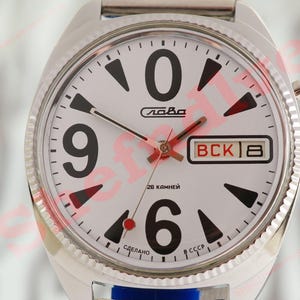 May include: Close-up of a vintage silver wristwatch with a white face. The watch features large black numerals, red hands, and a day-date display. The watch face has the word "Слава" and "CCCP" printed on it.