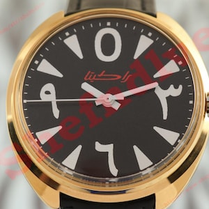 May include: A gold wristwatch with a black face displaying Arabic numerals and hands. The watch has a black leather strap and a gold bezel. The watch face features the Arabic text "راكتينا" in red.