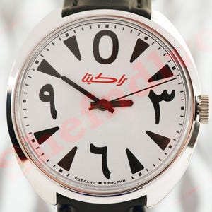 May include: A silver wristwatch with a white face. It features black Arabic numerals and red hands. The watch has a black leather strap and a winding crown. The watch face also has red text.