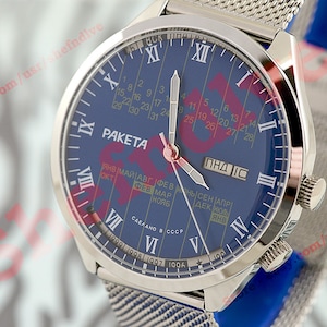 Puede incluir: Un reloj de pulsera plateado con una esfera azul y una correa de malla plateada. La esfera presenta un calendario con los días de la semana y el mes, y el texto "PAKETA" en rojo. El reloj fue fabricado en la URSS.