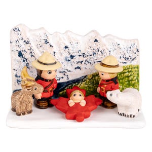 Puede incluir: Un bel&eacute;n navide&ntilde;o de cer&aacute;mica con tem&aacute;tica canadiense. Dos figuras vestidas como polic&iacute;as montados se encuentran junto a un beb&eacute; en una hoja de arce roja. Tambi&eacute;n se incluye un oso polar blanco y una cabra marr&oacute;n.