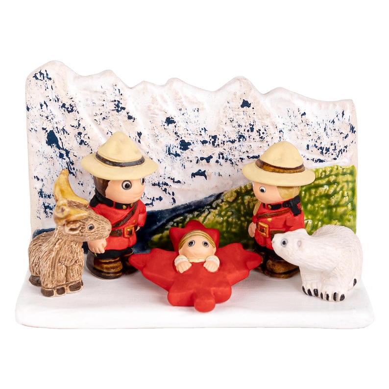 Puede incluir: Un bel&eacute;n navide&ntilde;o de cer&aacute;mica con tem&aacute;tica canadiense. Dos figuras vestidas como polic&iacute;as montados se encuentran junto a un beb&eacute; en una hoja de arce roja. Tambi&eacute;n se incluye un oso polar blanco y una cabra marr&oacute;n.