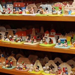 Puede incluir: Una colecci&oacute;n de figuritas en miniatura que representan diversas escenas y personajes. Las figuritas est&aacute;n hechas de cer&aacute;mica pintada y est&aacute;n dispuestas en estantes. Las figuritas incluyen una escena de la natividad, un grupo de ni&ntilde;os jugando y un grupo de personas con ropa tradicional.