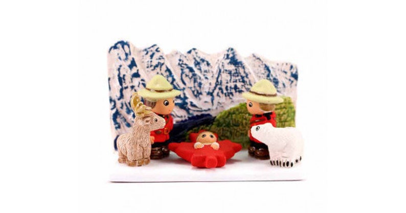 Puede incluir: Una escena de la natividad navide&ntilde;a con una hoja de arce roja, un oso polar blanco, un ciervo marr&oacute;n y dos figuras que llevan uniformes de guardabosques rojos y negros con sombreros amarillos. La escena est&aacute; ambientada en un fondo de una cordillera.