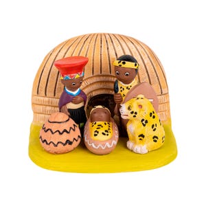 Puede incluir: Un belén en una cabaña con techo de paja marrón. Las figuras son de cerámica y están pintadas con colores vivos. Las figuras incluyen una madre, un padre, un bebé y un leopardo.