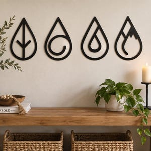 May include: Four black wall-mounted decorations shaped like teardrops, each featuring a unique internal cutout design representing a leaf, a swirling wave, a single smaller droplet, and a mountain peak, arranged horizontally on a light wall.