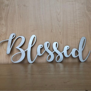 May include: Silver metal wall decor with the word "Blessed" in a cursive font.