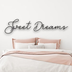 Może przedstawiać: Biała sypialnia z łóżkiem z różową kołdrą i białymi poduszkami. Ściana nad łóżkiem ma napisane „Sweet Dreams” czarnym, ozdobnym pismem.