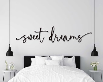 May include: A white bed with white bedding and black headboard in a white room with a black metal sign that says "sweet dreams" hanging above the headboard.