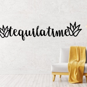 May include: Black wall decor with the text "tequilatime" in cursive script, flanked by two stylized agave plant illustrations. The decor is displayed in a living room setting with a white armchair and a wooden side table.