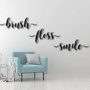 May include: Black cursive lettering on a white wall reads "brush floss smile" with a light blue armchair in the foreground.