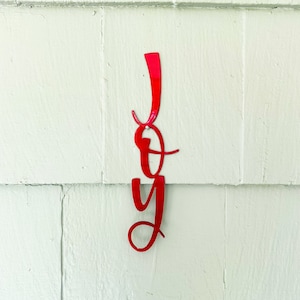 May include: Red metal JOY sign hanging on a white wall.