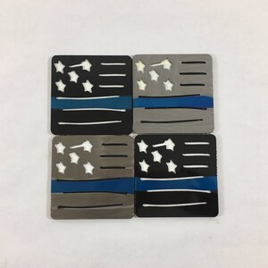 May include: Four coasters featuring a thin blue line American flag design. Two coasters are black with white stars and two coasters are gray with white stars.