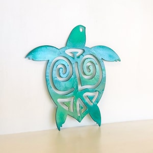 Puede incluir: Una decoración de pared de metal de color azul turquesa en forma de tortuga con un patrón de espiral. La tortuga está cortada de metal y tiene una parte posterior plana.