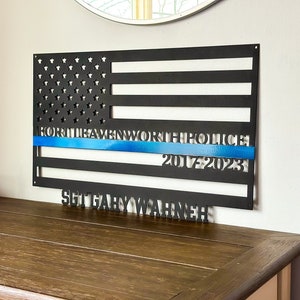 May include: Black metal American flag with a blue line and the text "North Havenworth Police 2017-2023" and "Sgt Gary Warner" below.