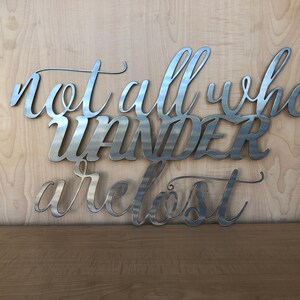 May include: Metal wall art with the quote "Not all who wander are lost". The quote is written in a cursive font and is made of silver metal.