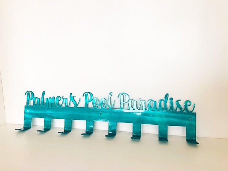 May include: Teal metal wall hook with the text "Palmers Pool Paradise" and eight hooks.