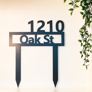 May include: Black metal yard sign with the address 1210 Oak St. The sign is attached to two metal stakes.
