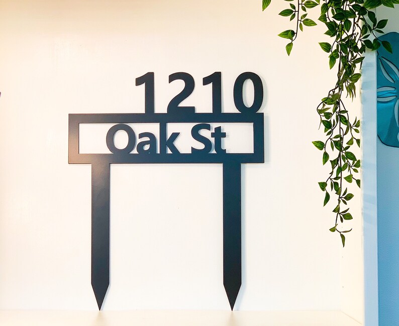 May include: Black metal yard sign with the address 1210 Oak St. The sign is attached to two metal stakes.